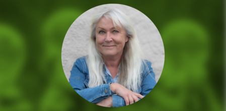 Kvinna med långt vitt hår och jeansjacka sitter framför en ljus bakgrund och ler mot kameran.