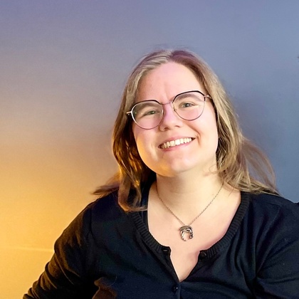 Två leende personer sitter tillsammans i en blå soffa i ett rum med blå vägg och grön växt.