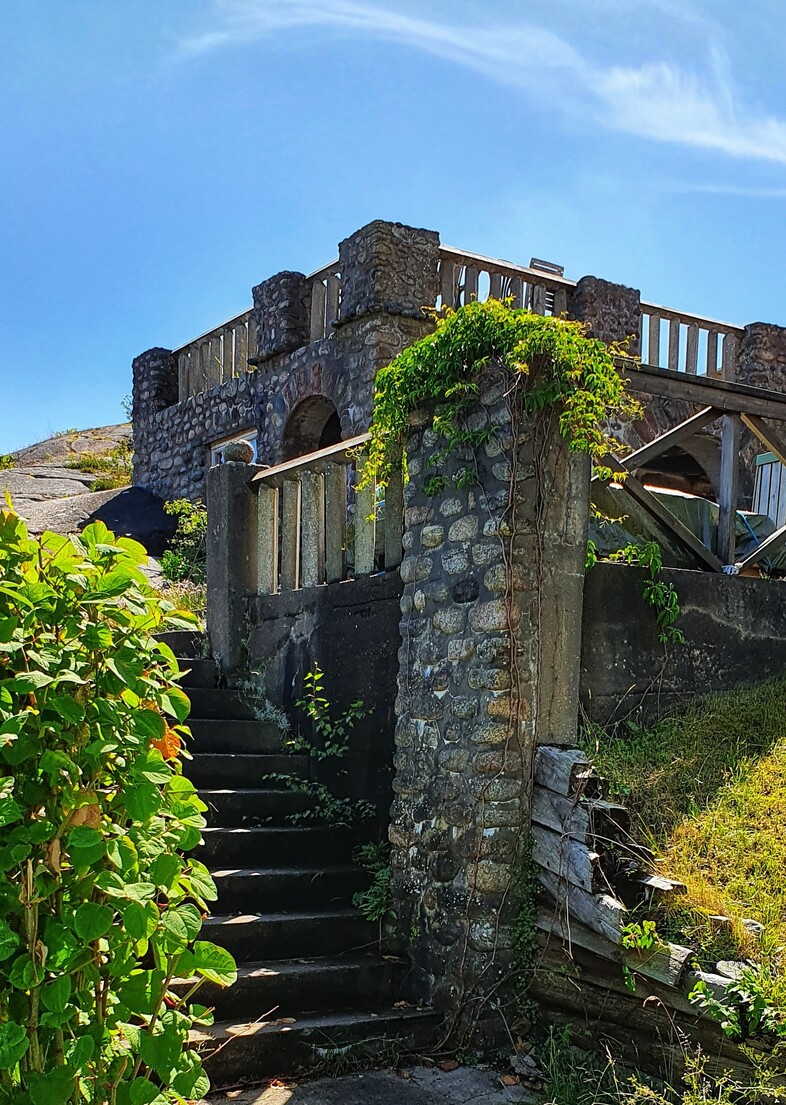 Stenbyggnad med trappa och grönska under en klarblå himmel.