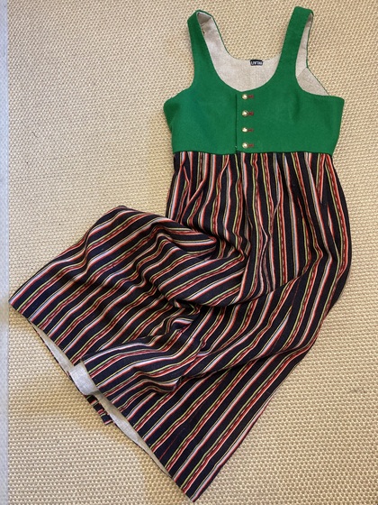 En klänning med grön överdel och randig kjol i svart, rött, gult och grönt ligger på ett ljust golv.