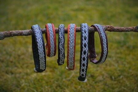 Sex armband med flätade mönster hänger på en gren utomhus med gräs i bakgrunden.