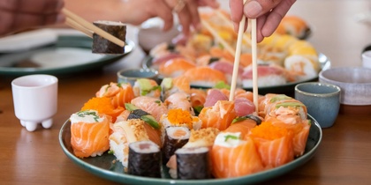 Två personer plockar sushi med ätpinnar från ett fat på ett matbord.