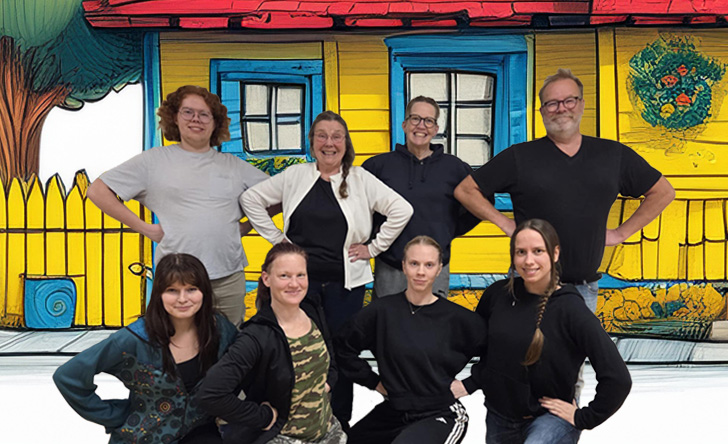 En grupp människor i olika åldrar står framför ett hus i glada färger.