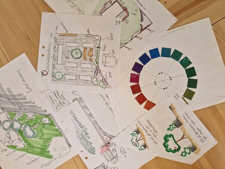 Flera handritade skisser och planer för trädgårdsdesign ligger utspridda på ett trägolv.