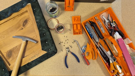 Arbetsbänk med verktyg, skruvar, hammare och en träskiva med tyg, redo för möbelrenovering.