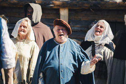 En grupp människor i historiska kläder står utomhus framför en träbyggnad.