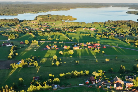 Landskapsvy över gröna fält, gårdar och en sjö i bakgrunden, fotograferat från ovan i kvällssol.