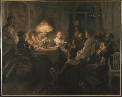 En grupp människor sitter samlade runt ett bord i ett svagt upplyst rum, några lyssnar på en kvinna som läser högt.