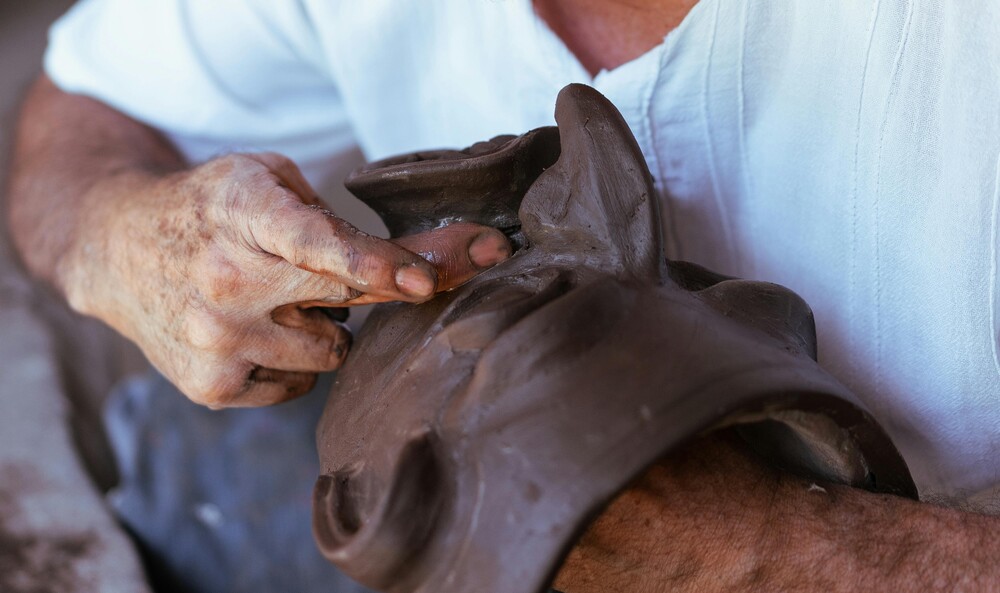 En person formar en lerfigur med händerna, klädd i vit skjorta.