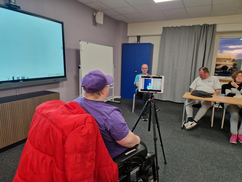 Person i rullstol med röd jacka deltar i möte med tre andra personer i ett konferensrum.