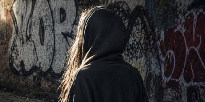 Person med huva står med ryggen mot kameran framför en vägg med graffiti utomhus.