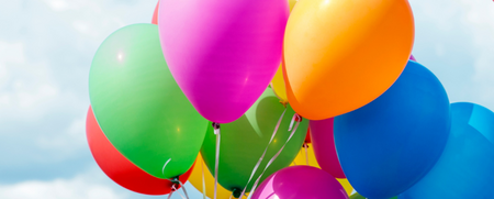 Flera färgglada ballonger svävar mot en blå himmel med vita moln.
