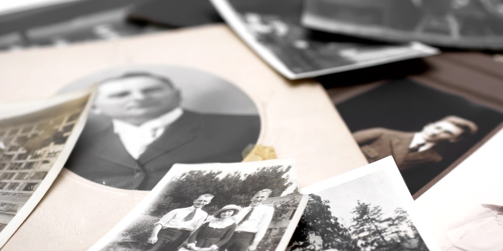 En hög med gamla svartvita fotografier, flera visar människor och familjer utomhus och inomhus.