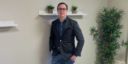 En person står vid väggen i ett mötesrum med bord, stolar, växter och hyllor med krukväxter.