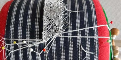 En spetskudde med påbörjad knyppling, träpinnar och trådar syns tydligt.