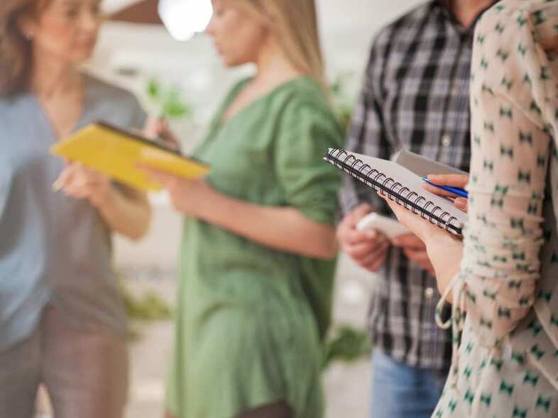 Personer står och samtalar och läser från anteckningsblock.