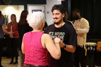 Två personer dansar tillsammans i ett rum med andra människor i bakgrunden.