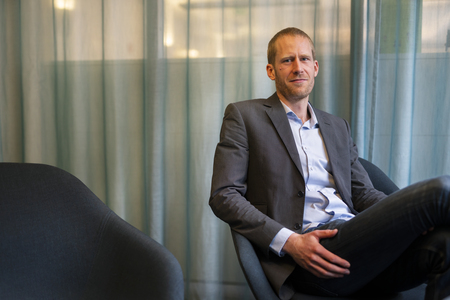 Linus Olofsson sitter avslappnat i en fåtölj framför ett blågrönt draperi.