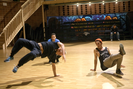 Tre unga personer dansar breakdance i en dansstudio med trägolv och graffitimålning på väggen.