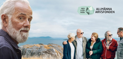 En äldre man med vitt skägg tittar mot kameran, i bakgrunden står fem personer vid havet och pratar.