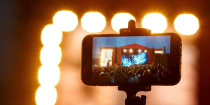 En smartphone på stativ filmar en konsert med starka scenljus i bakgrunden.