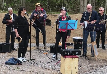 Ett band spelar musik utomhus med flera instrument och två sångare vid mikrofoner.