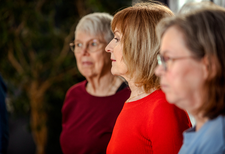 Tre äldre kvinnor står i profil, fokuserade på något utanför bild.