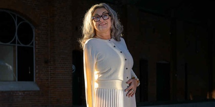 Kvinna i ljus kjol och tröja står på en perrong med tegelvägg och stora fönster i bakgrunden.