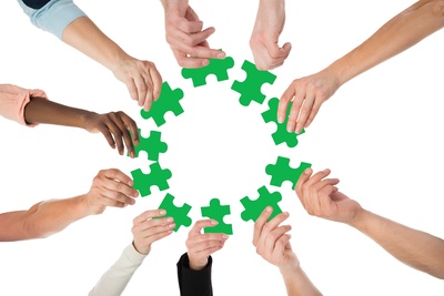 Flera händer håller gröna pusselbitar i en cirkel mot en vit bakgrund.