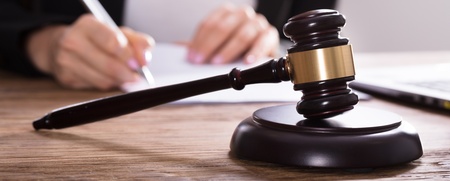 En domarklubba ligger på ett skrivbord medan en person skriver på papper i bakgrunden.