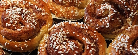 Nygräddade kanelbullar med pärlsocker ligger på ett galler, delvis täckta av en vit kökshandduk.