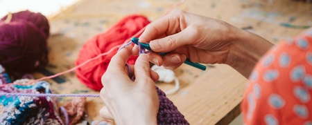 Två personer sitter vid ett bord och stickar med färggarn, händerna i fokus.