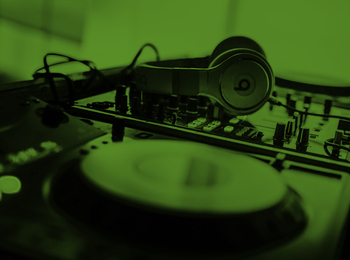 Ett DJ-mixerbord med hörlurar placerade ovanpå, belyst i grönt ljus.