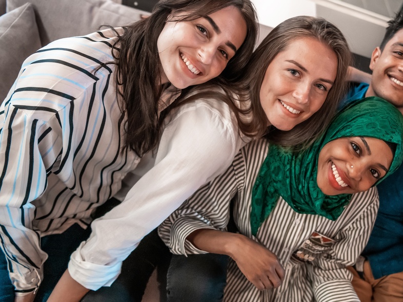 Fem unga vuxna sitter tillsammans på en soffa och ler mot kameran.