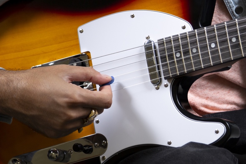 En person spelar elgitarr med en plektrum, närbild på händer och gitarr.