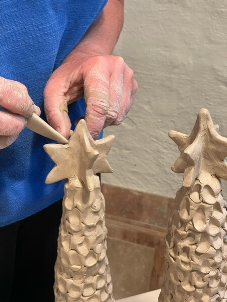 En person formar en stjärna av lera på toppen av en konformad skulptur med ett verktyg.