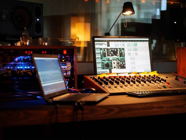 Ett inspelningsstudio med mixerbord, dator, skärm och ljudutrustning på ett träbord.
