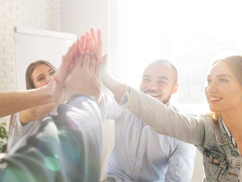 Fem personer sitter i en ring och sträcker fram sin ena arm och klappar mot varandras händer.