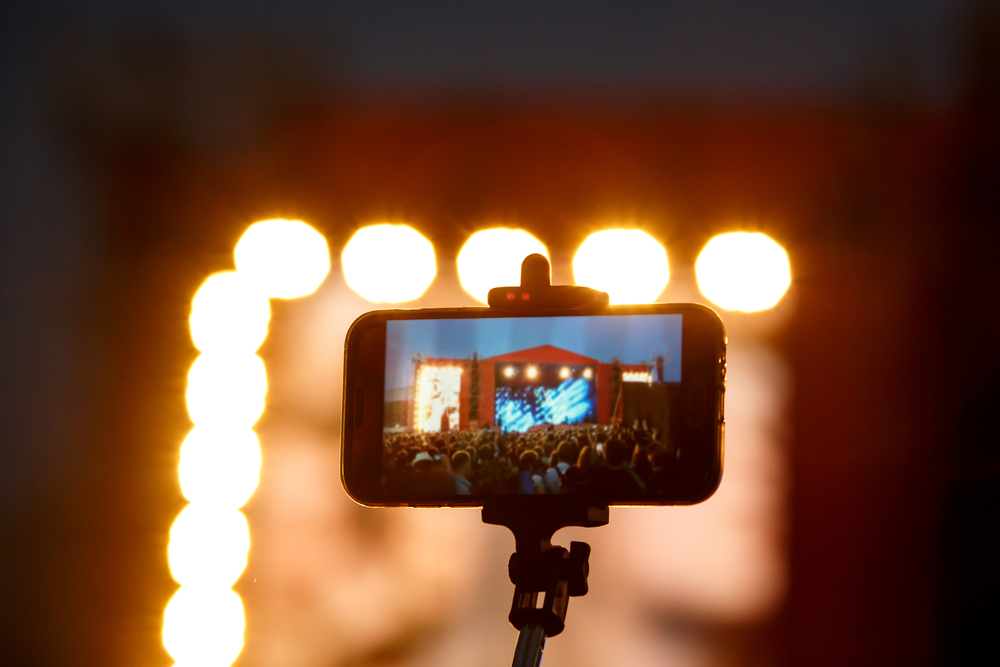 En smartphone på stativ filmar en konsert med starka scenljus i bakgrunden.