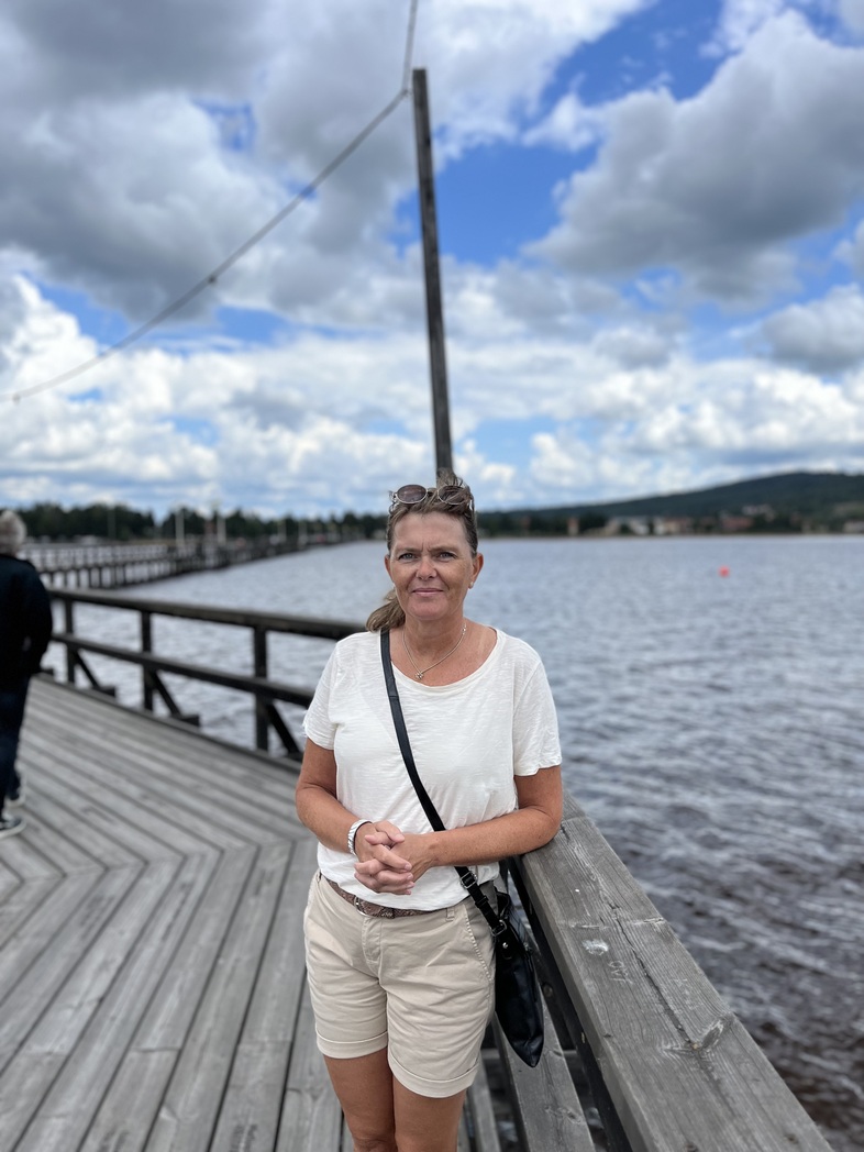 Anna Anteryd i vit t-shirt och beige shorts står på en brygga vid vattnet under en molnig himmel.