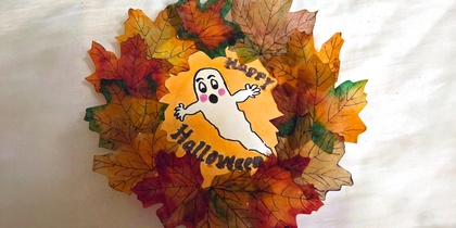 En Halloween-dekoration med färgglada höstlöv och en tecknad spöke med texten 'Happy Halloween'.