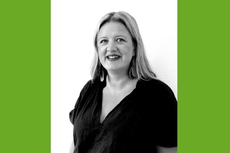 Kvinna med axellångt hår och mörk tröja ler mot kameran, svartvit bild med grön bakgrund.