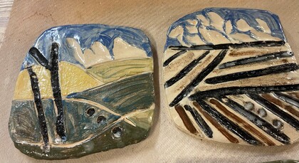 Två keramiska plattor med abstrakta landskapsmotiv i blått, grönt, gult och svart.