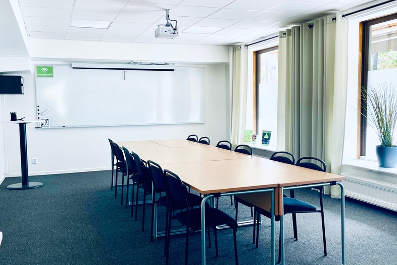 Ljust konferensrum med långbord, svarta stolar, stora fönster och whiteboard.