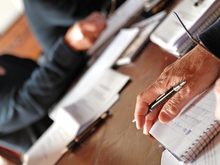 Flera personer sitter vid ett bord och skriver i anteckningsblock med papper och pennor.