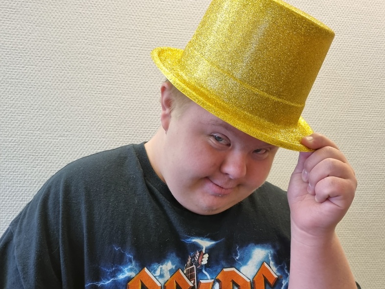 Person med svart AC/DC-tröja och glittrig gul hatt håller hatten med ena handen. Ansiktet är dolt.