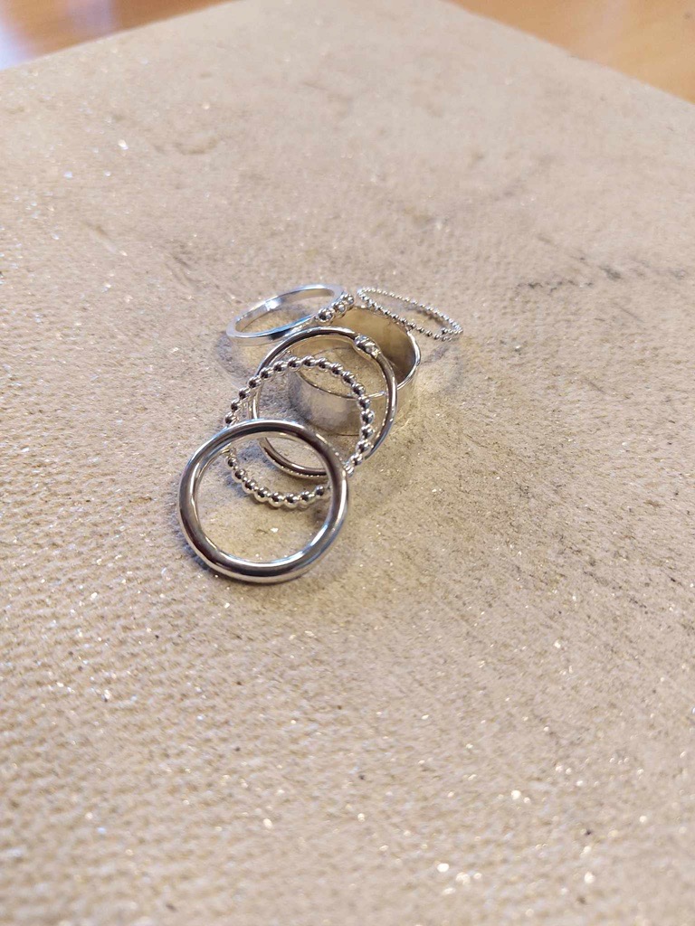 Fem silverringar ligger på en beige, glittrig tygyta.