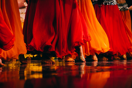Flera personer dansar barfota i färgglada, flödande kjolar i rött och orange på en scen.