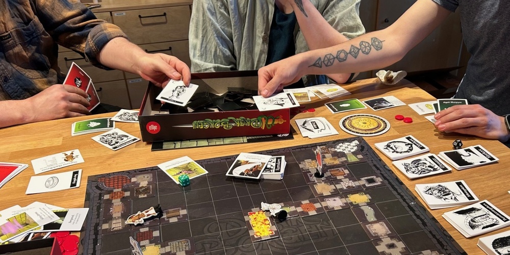 Tre personer spelar ett brädspel med kort och marker på ett träbord.