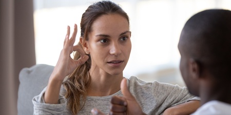 Två personer kommunicerar med teckenspråk i ett ljust vardagsrum.